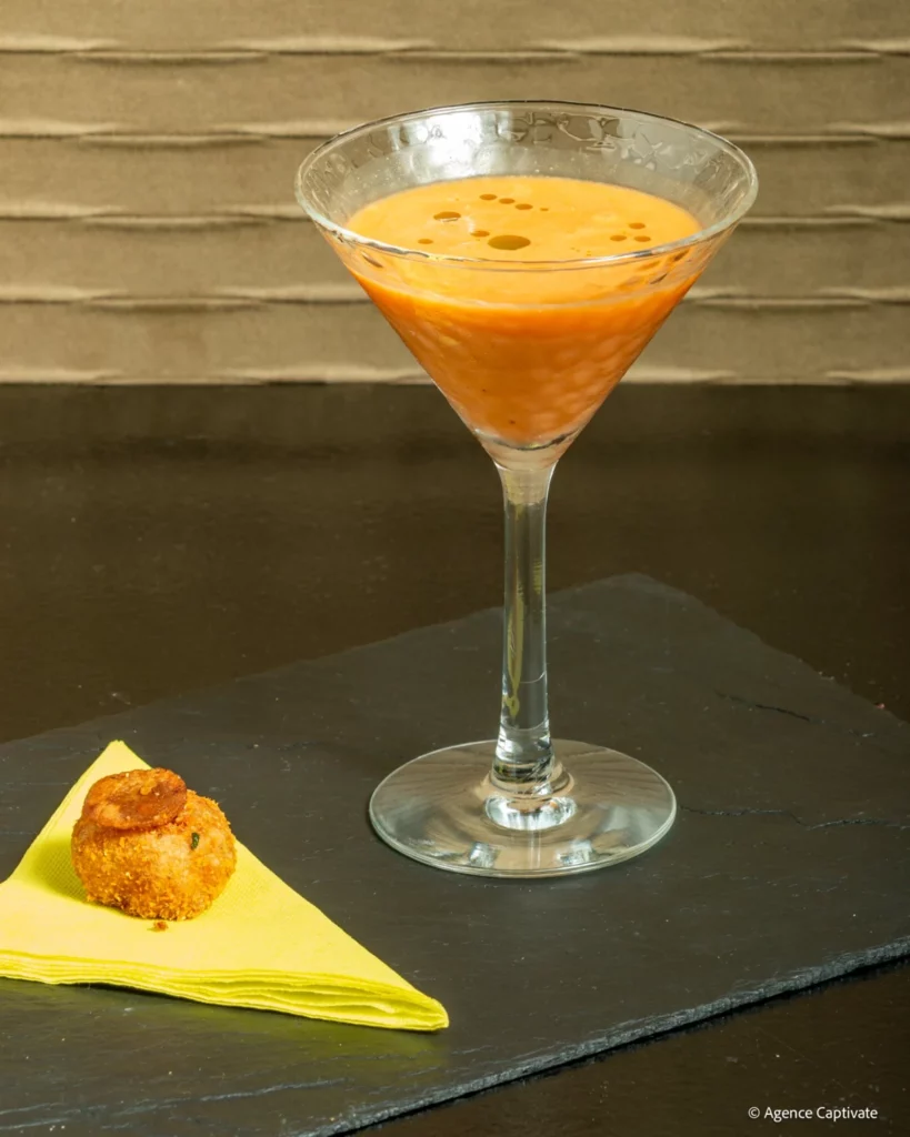 Cocktail orangé en verre à pied, accompagné d’une bouchée sur ardoise